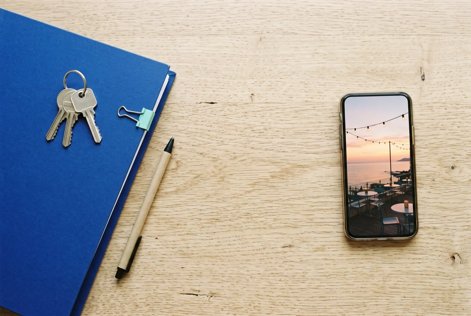 Su un tavolo di legno, le chiavi di una casa nuova sopra una cartellina di documenti e, accanto, uno smartphone con la foto di una terrazza sul mare al tramonto